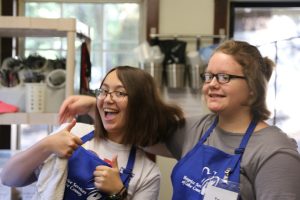 two teen junior volunteers helping in the camp kitchen. both are smiling and one is giving an enthusiastic thumbs up!